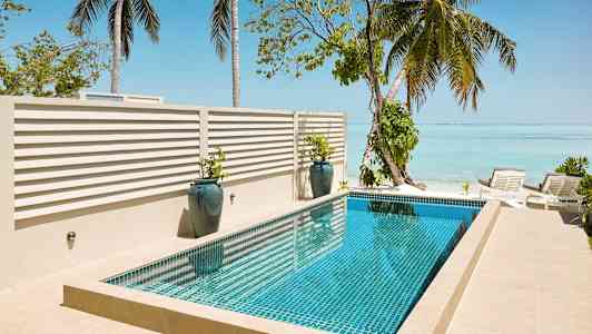 Et basseng ved sjøen omgitt av palmer og solsenger. (AI-generert tekst)