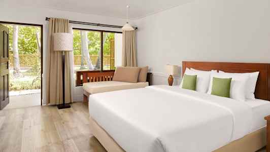 Et hotellrom med en dobbeltseng, sitteplass og et vindu som vender mot grønne trær. (AI-generert tekst)