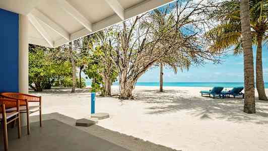 En sandstrand med noen solsenger, palmer og et blått hav i bakgrunnen, sett fra en uteplass. (AI-generert tekst)