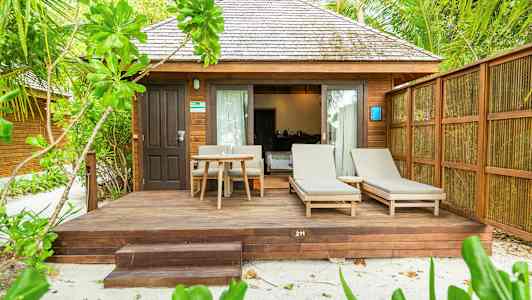 En bungalow med trepanel, terrasse med solsenger og bord, omgitt av grøntområder. (AI-generert tekst)