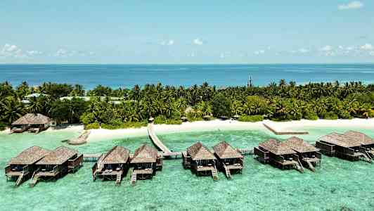 Luksuriøse bungalower på påler over klart turkist vann og en tropisk strand med palmer. (AI-generert tekst)