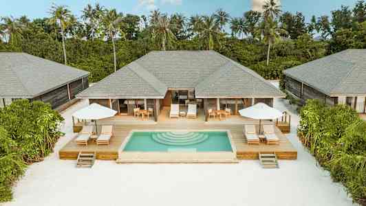 Villaer med private bassenger og solterrasser omringet av grønne omgivelser ved en hvit sandstrand. (AI-generert tekst)