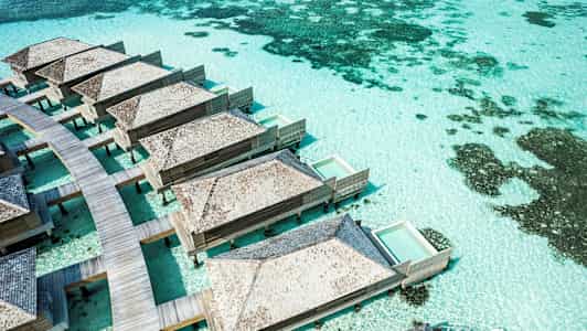 Bungalower på påler med private bassenger over turkist vann. (AI-generert tekst)