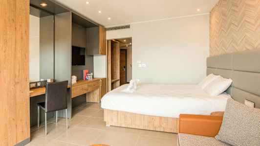 Et hotellrom med en dobbeltseng, skrivebord og et sitteområde. (AI-generert tekst)