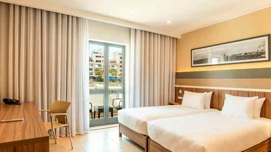 Hotellrom med to enkeltsenger, skrivebord og en balkong med glassdører. (AI-generert tekst)