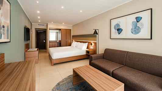 Et hotellrom med en dobbeltseng, sofa, bord og veggkunst. (AI-generert tekst)