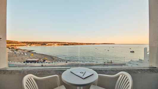 Utsikt fra en balkong mot en sandstrand og havet ved solnedgang. (AI-generert tekst)