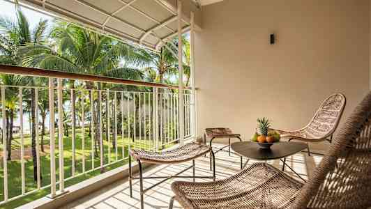 En møblert balkong med utsikt over en hage med palmer. (AI-generert tekst)