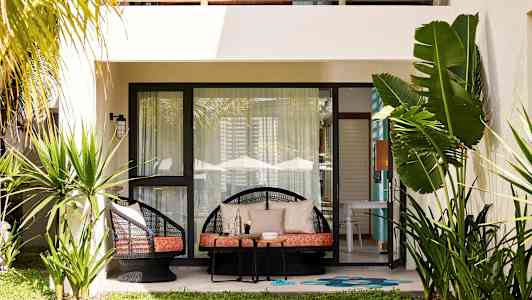 En terrasse med lenestoler, bord og planter foran en bolig. (AI-generert tekst)