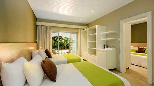 Hotellrom med to senger, grønne sengetepper og utsikt mot hagen. (AI-generert tekst)