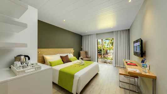 Hotellrom med dobbeltseng, skrivebord og balkong med utsikt over trær og vegetasjon. (AI-generert tekst)