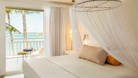 En lys hotellsuite med himmelseng og utsikt over havet fra balkongen. (AI-generert tekst)