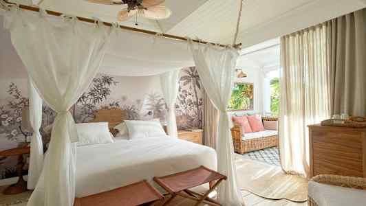 Et soverom med en himmelseng, veggdekor og innredning med lyse møbler samt en sittegruppe ved vinduet. (AI-generert tekst)