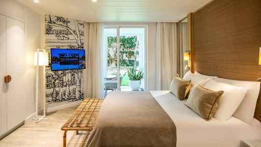 Hotellrom med dobbeltseng, sittemøbler utendørs ved døren og veggmontert TV. (AI-generert tekst)