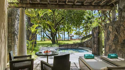 En terrasse med sitteplasser og solsenger ved siden av et lite basseng, omgitt av planter og med utsikt mot stranden og palmetrær. (AI-generert tekst)