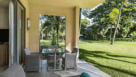 Utsikt fra en terrasse med hagemøbler mot grøntområde og palmer. (AI-generert tekst)