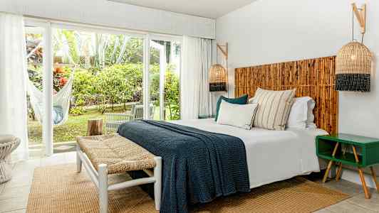 Et soverom med dobbeltseng, tredetaljer og store vinduer mot en grønn utsikt. (AI-generert tekst)