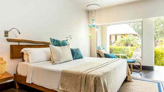 Et lyst soverom med en dobbeltseng og store vinduer ut mot en frodig hage. (AI-generert tekst)