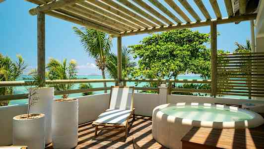 En tredekk med en solseng, tre hvite blomsterpotter og et boblebad, med utsikt over havet og omkringliggende palmer. (AI-generert tekst)