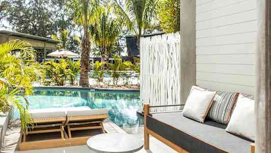 Utendørsområde med basseng, solsenger og en sofa med puter. (AI-generert tekst)