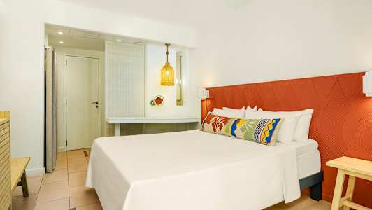 Hotellrom med en dobbeltseng, fargerik pute og en oransje sengegavl. (AI-generert tekst)