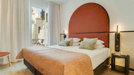 Moderne hotellrom med dobbeltseng, rødt sengegavl og store vinduer mot en balkong. (AI-generert tekst)