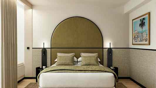 Et hotellrom med en seng, grønne puter og et innrammet bilde på veggen. (AI-generert tekst)