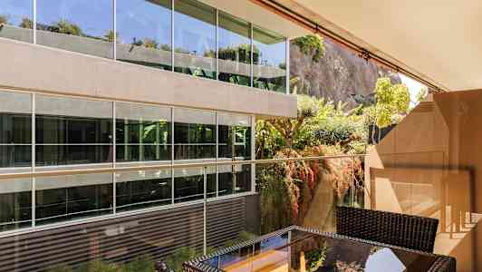 Uteplass med møbler foran en moderne glassbygning ved en frodig fjellvegg. (AI-generert tekst)