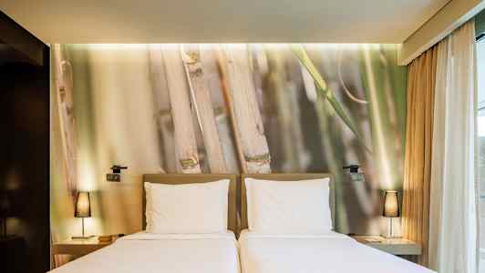 To enkeltsenger med hvite laken foran en vegg med bambusmotiv. (AI-generert tekst)