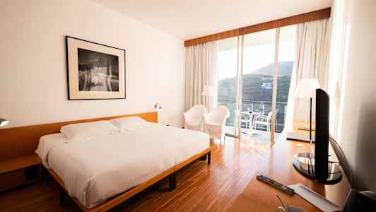 Et hotellrom med en dobbeltseng, et skrivebord, to stoler og en terrasse med utsikt. (AI-generert tekst)