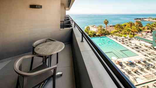 Balkong med bord og stoler med utsikt over et basseng og havet. (AI-generert tekst)