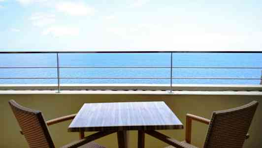En utendørs terrasse med et bord og to stoler, med utsikt over havet. (AI-generert tekst)