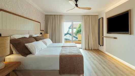 Et hotellrom med to senger dekket med hvitt og beige sengetøy. Det er en takvifte, et stort vindu med utsikt og en veggmontert TV. (AI-generert tekst)