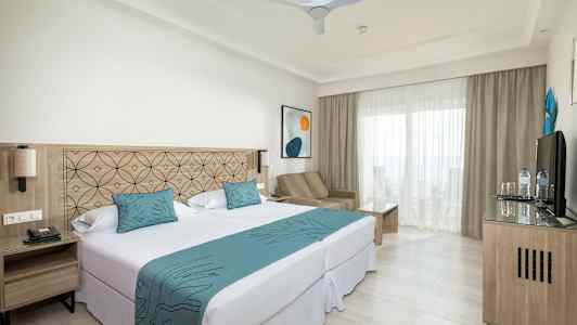 Bilde av et hotellrom med dobbeltseng, sittegruppe og balkong. (AI-generert tekst)