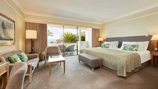 Et hotellrom med stor seng, sittegruppe og en balkong med utsikt. (AI-generert tekst)