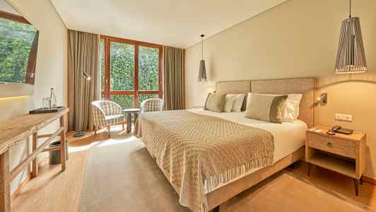 Et hotellrom med en bred seng, to lenestoler ved et vindu og et bord. (AI-generert tekst)