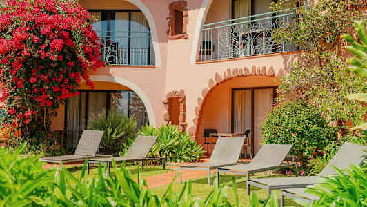 En bygning med buede balkonger omgitt av grøntområder og blomster, med solsenger på gressplenen. (AI-generert tekst)