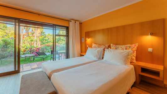 Et hotellrom med to enkeltsenger, myke puter og et stort glassvindu som vender mot en hage. (AI-generert tekst)