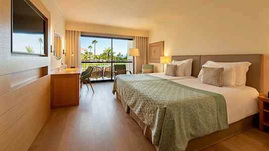 Moderne hotellrom med dobbeltseng og balkong i bakgrunnen. (AI-generert tekst)