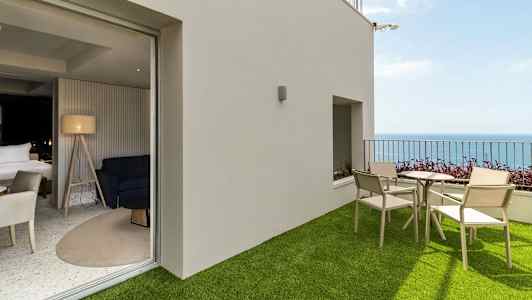 En terrasse med kunstgress, bord og stoler samt havutsikt, tilkoblet et moderne rom med interiør. (AI-generert tekst)