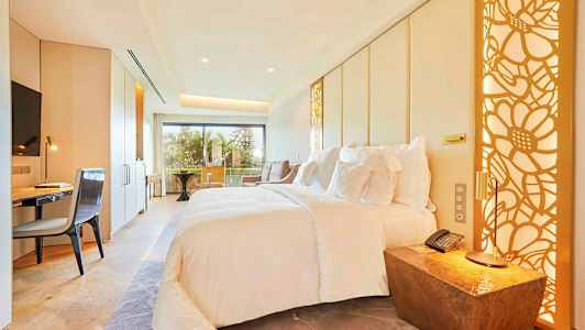 Et moderne hotellrom med en stor seng, skrivebord, stol og balkong med utsikt. (AI-generert tekst)