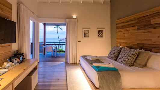 Et hotellrom med en stor seng og utgang til en terrasse med utsikt over havet. (AI-generert tekst)