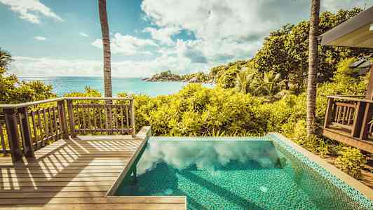 Utsikt fra en treterrasse og et basseng over en tropisk hage og havet. (AI-generert tekst)