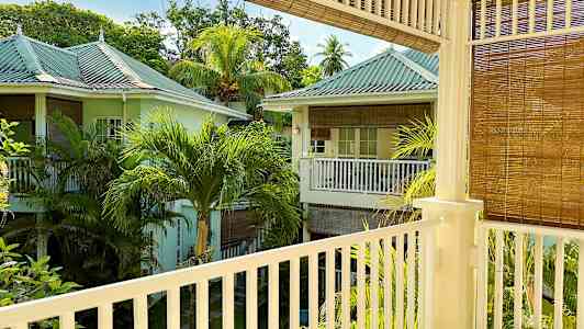 En utsikt fra en balkong som viser et frodig område med pastellfargede hus og palmetrær. (AI-generert tekst)