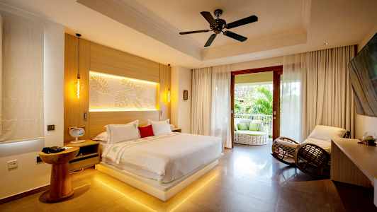 Et moderne soverom med en stor seng, sitteplasser og en åpen balkong med utsikt over grøntområder. (AI-generert tekst)