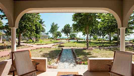 Utsikt fra en veranda mot en velstelt hage med gangveier og trær. (AI-generert tekst)