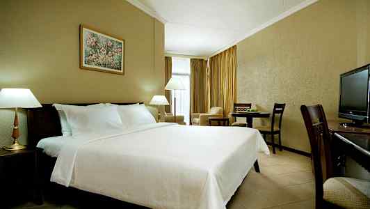 Et hotellrom med en stor oppredd seng, lamper, spisebord og en TV. (AI-generert tekst)