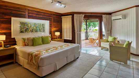 Et hotellrom med varme toner, en seng, sittemøbler og en terrasse med utsikt over grøntområder. (AI-generert tekst)