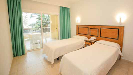 Hotellrom med to enkeltsenger, en liten uteplass med møbler og utsikt til palmetrær. (AI-generert tekst)