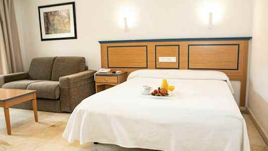 Hotellrom med oppredd seng og sofa. (AI-generert tekst)